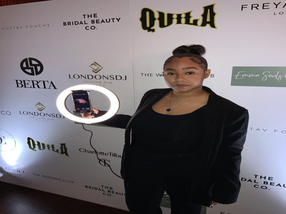 Guest photographed in front of a branded step-and-repeat backdrop featuring partner logos